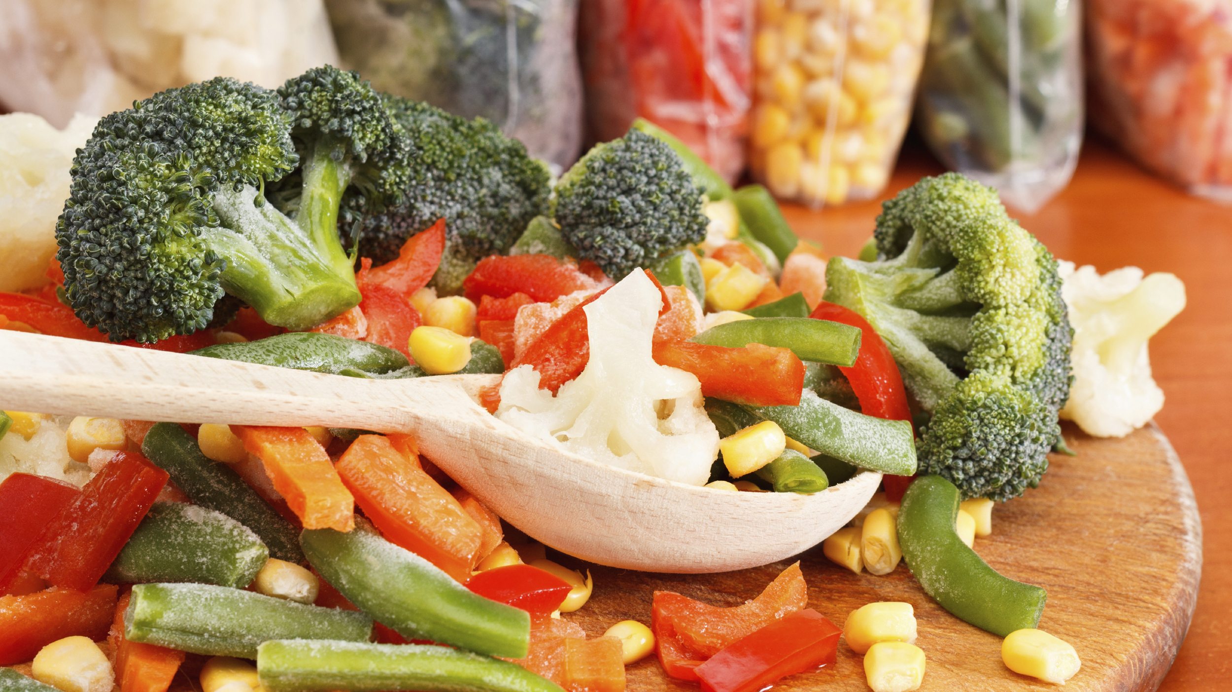 Mixed frozen vegetables on wooden cutting board and plastic bags