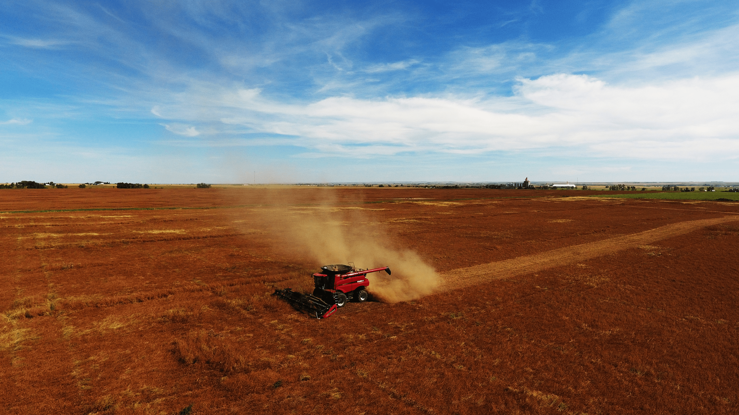 Red combine in a brown field with a bright blue sky