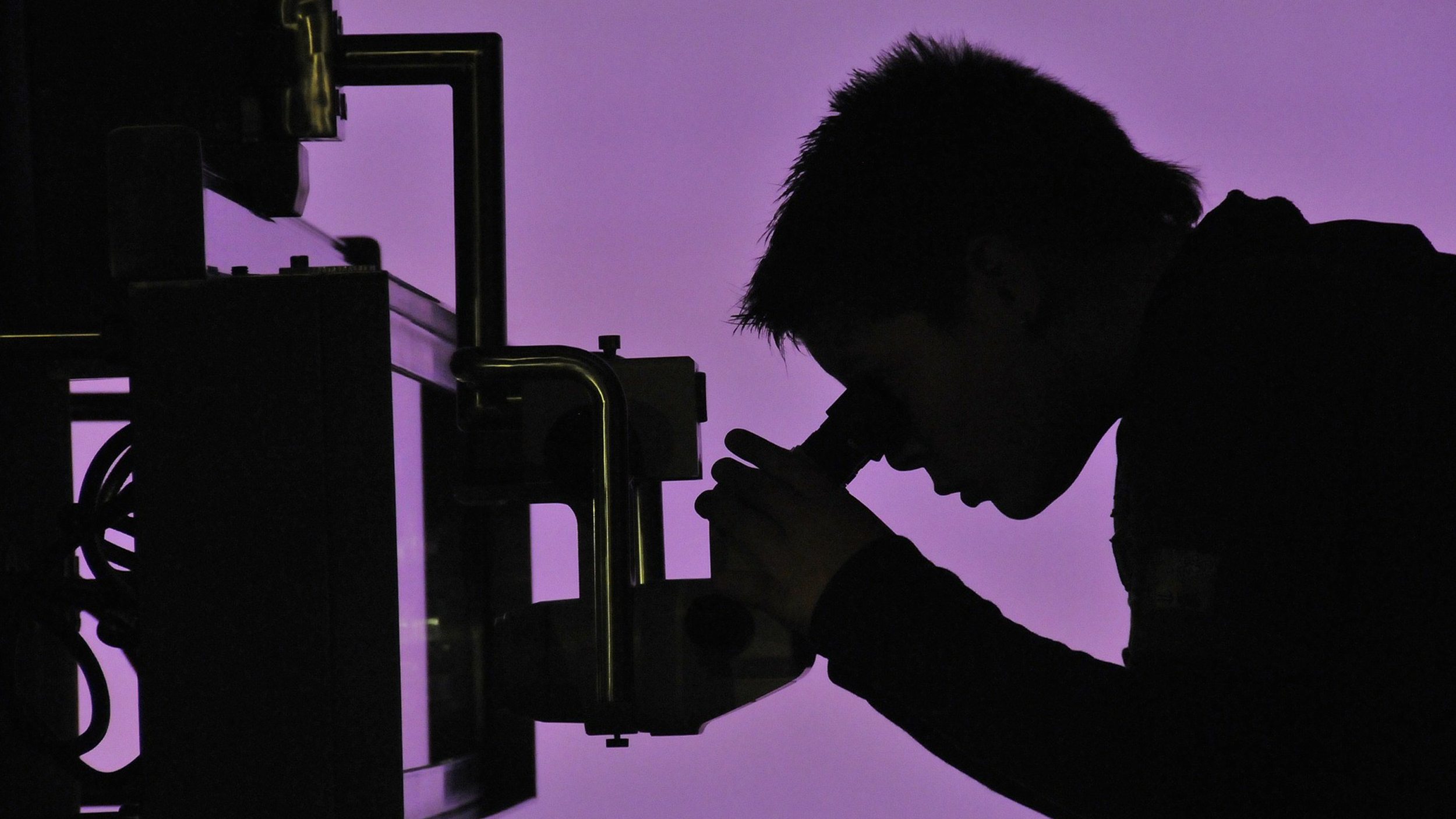 A silhouette of a man looking in a microscope at microbes