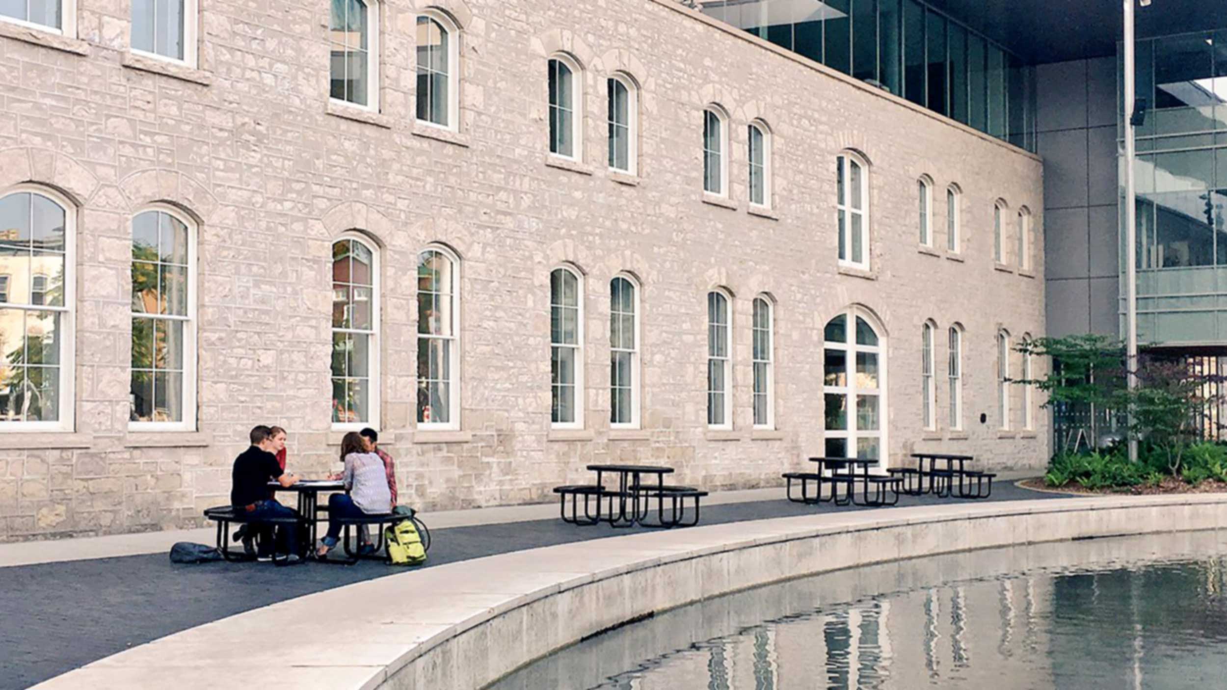 Students talk about ideas while sitting at a picnic table in front of an old building