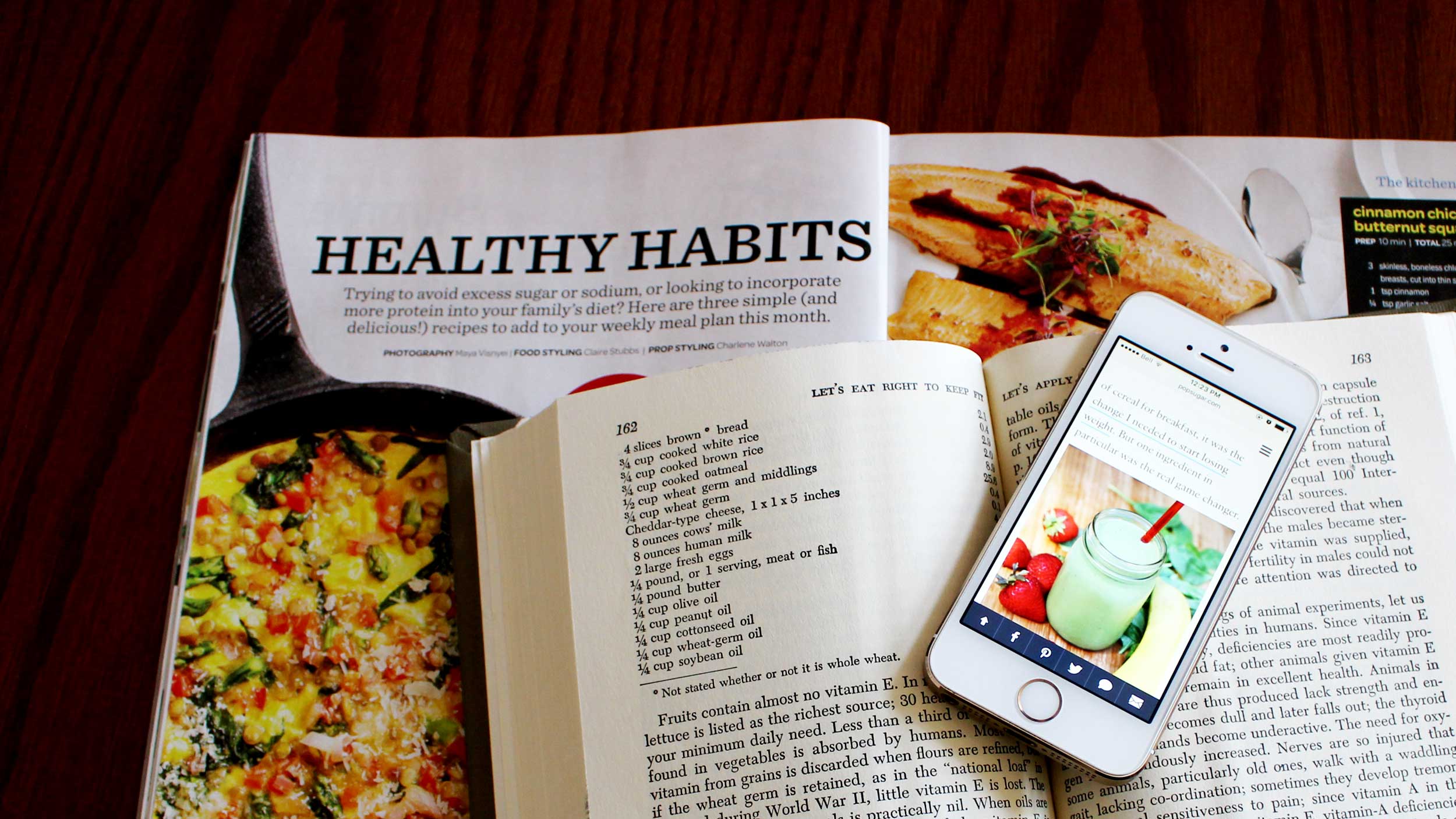 A phone sits on a cookbook and magazine about food
