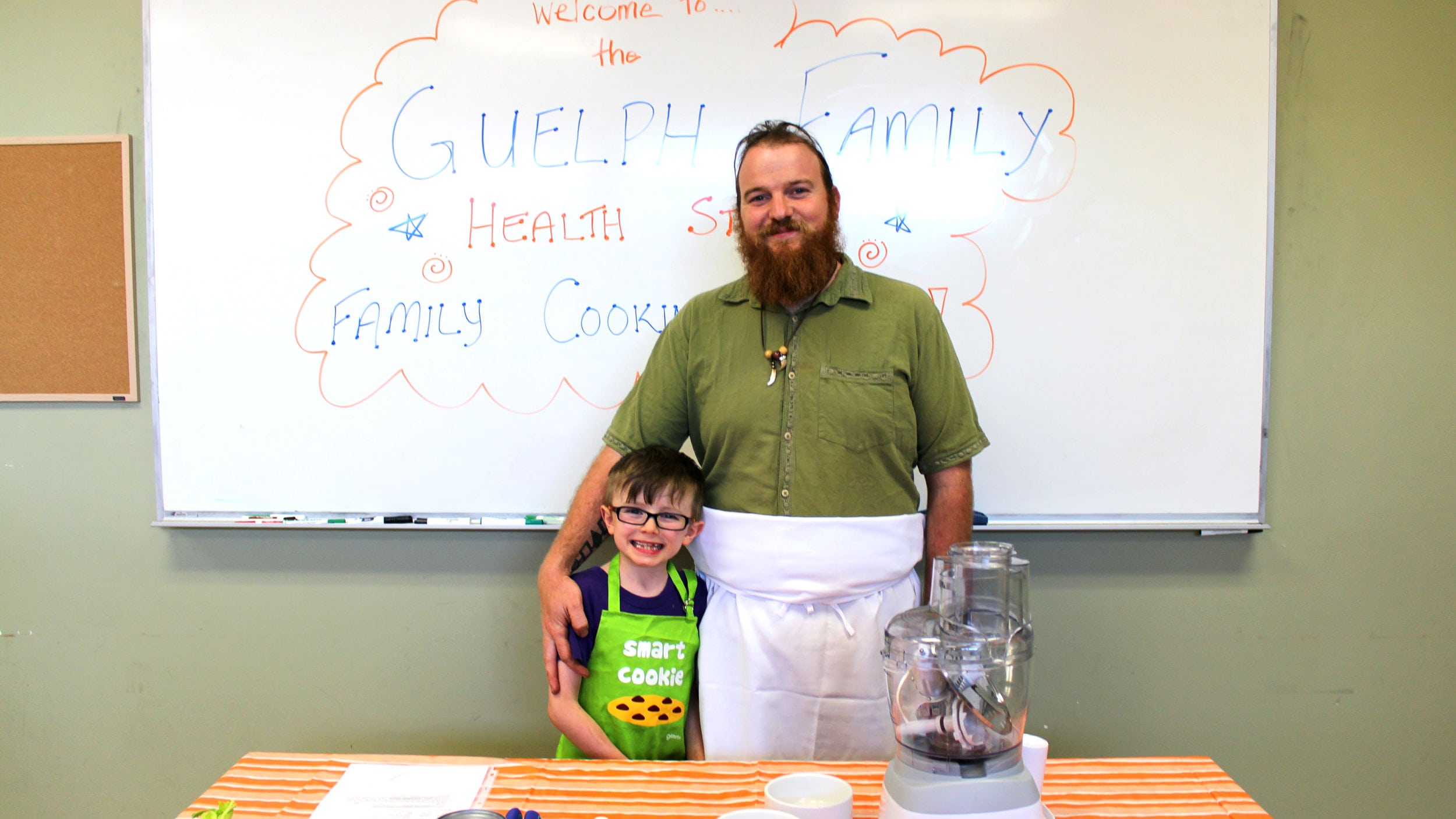 A father and son stand at a table preparing to cook