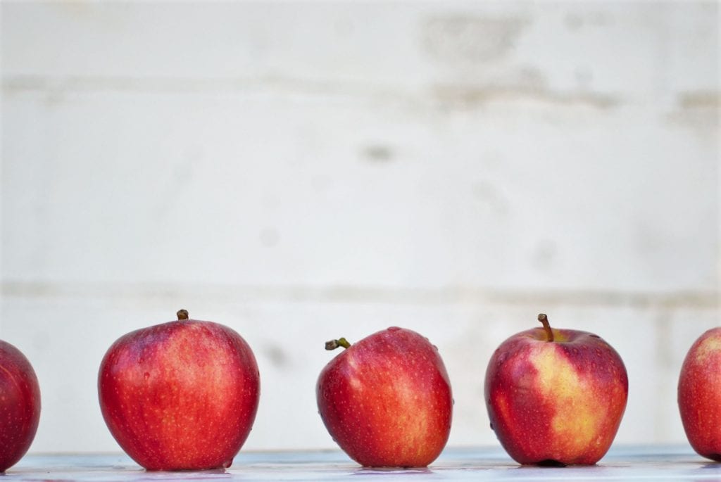 5 red apples lined up on a white surface