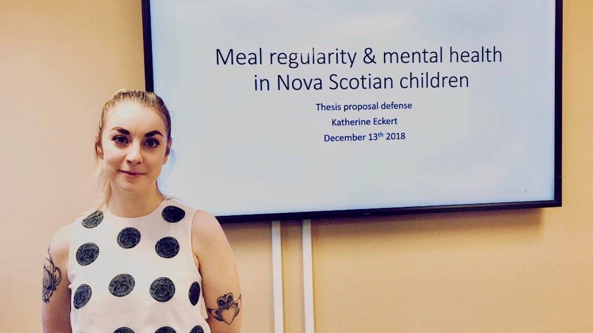 Katherine poses in front of screen showing the title of her presentation, "Meal regularity and mental health in Nova Scotian children"