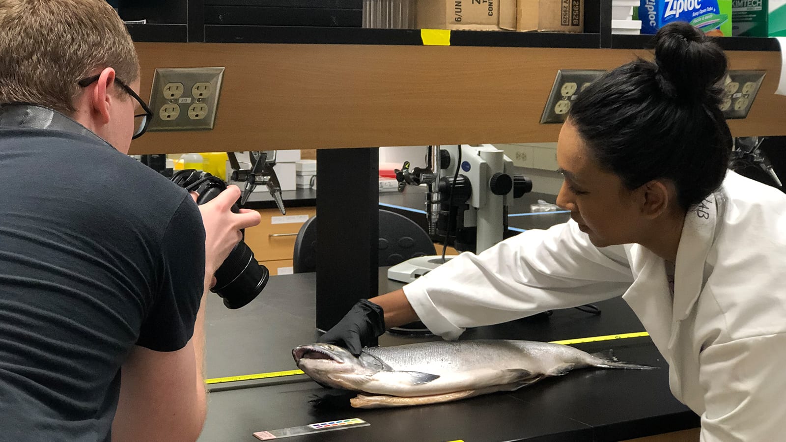 Maleeka holds a specimen for a photographer in a lab