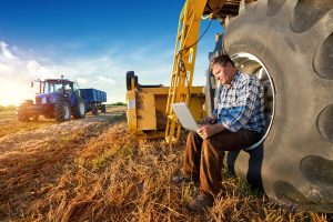 Farm worker on computer in field with mechanical equipment.